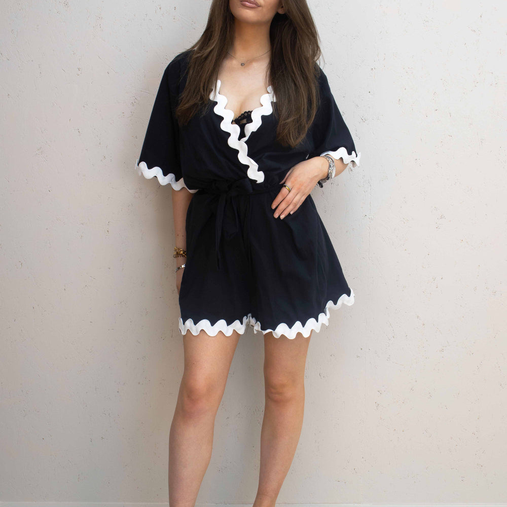 Lady wearing black coloured playsuit with white wavey piping design, complimenting the clothing with a pair of black chunky slip on sliders