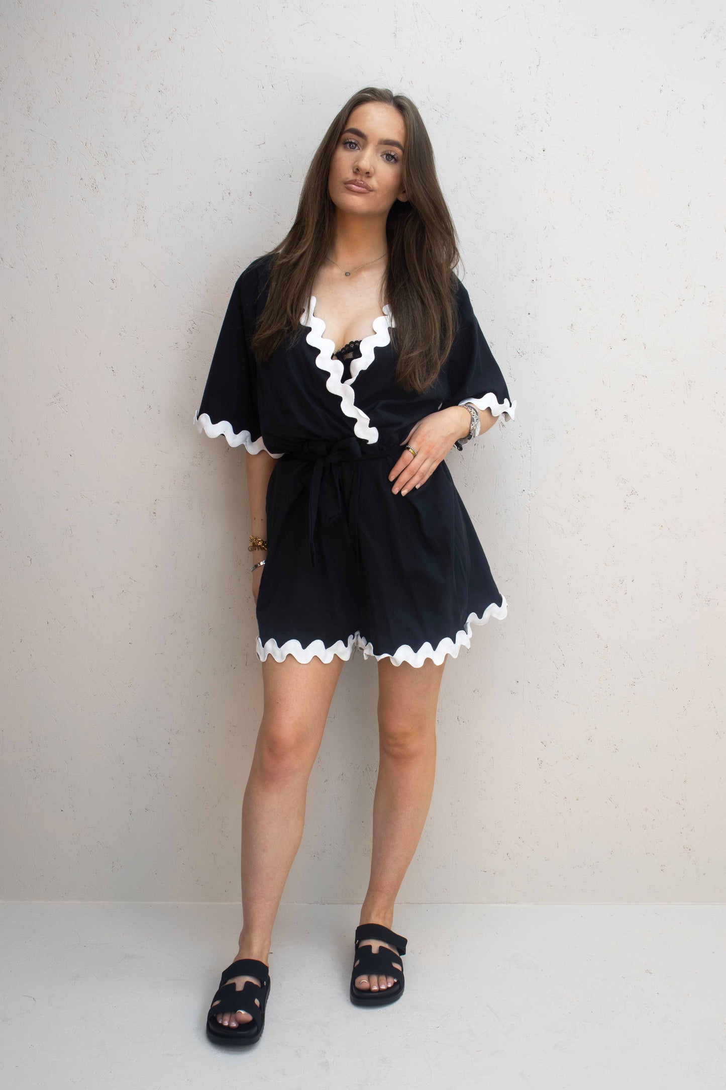 Lady wearing black coloured playsuit with white wavey piping design, complimenting the clothing with a pair of black chunky slip on sliders